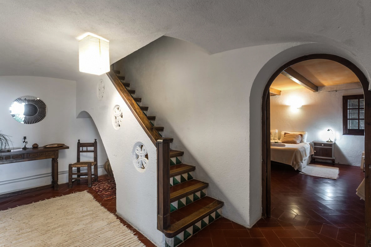Whitewashed hallway with a wooden staircase and arched doorway